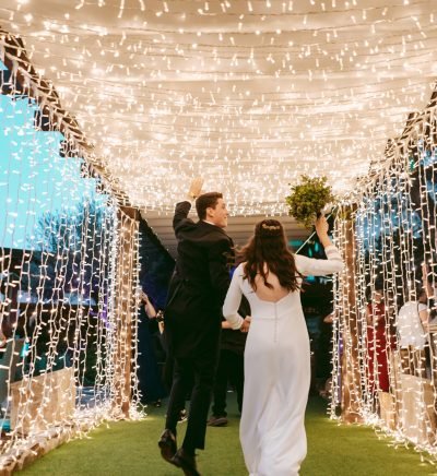 planificacion-bodas-urbanas-madrid Pareja entrando a la celebración bajo iluminación decorativa diseñada por azulymalva